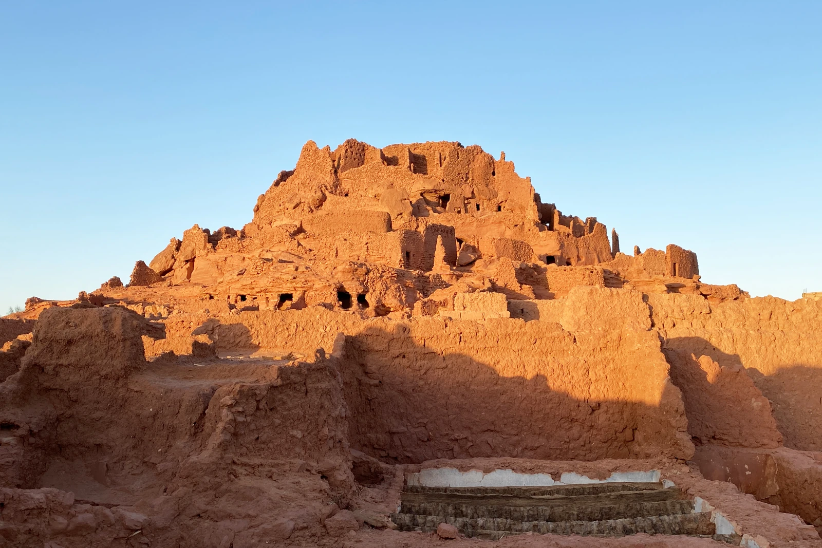 Ruines en terre ocre du ksar d’Ighzer sur une butte, dans la commune d’Ouled Saïd, avec des marches au premier plan.