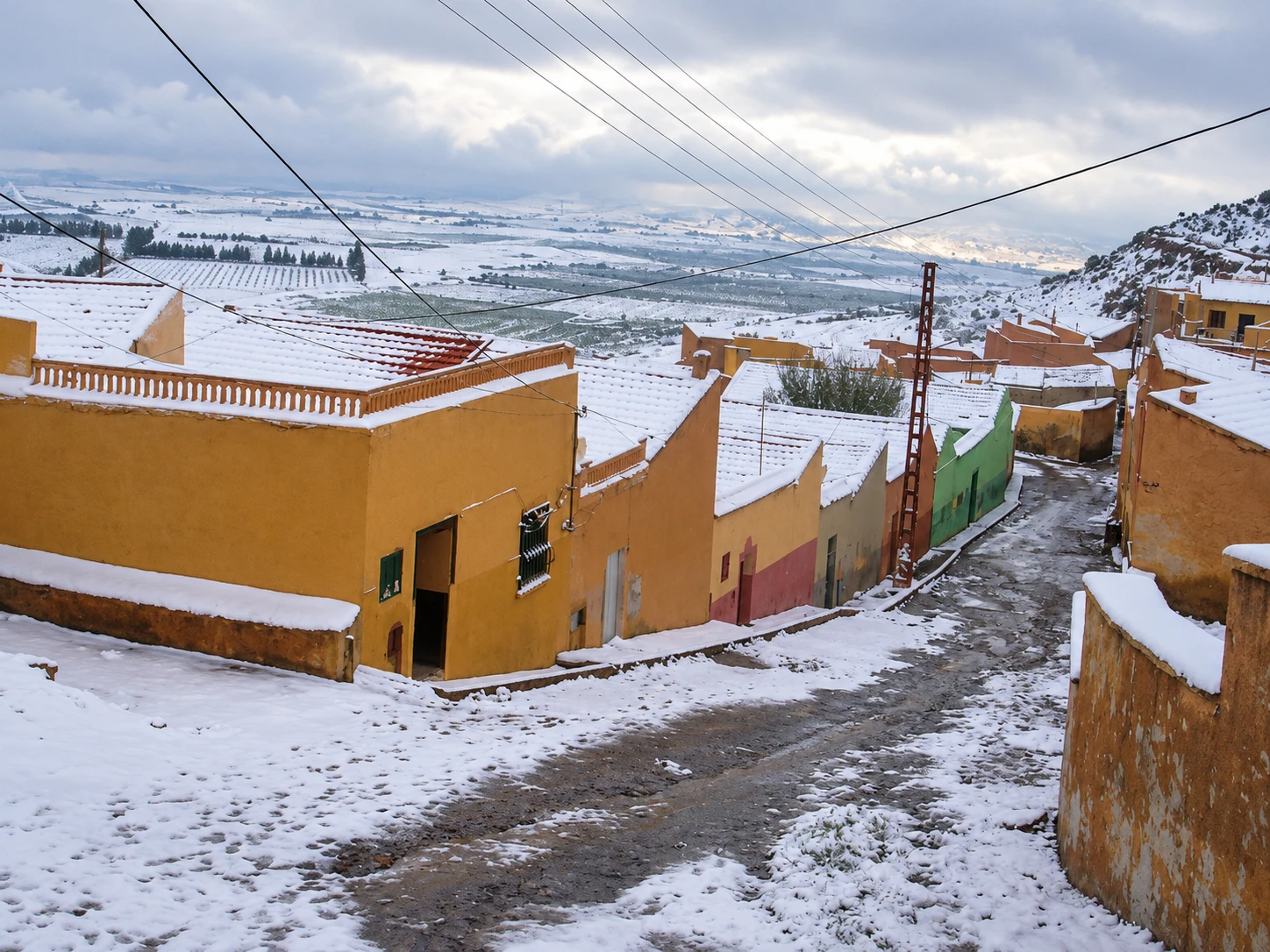Rue en pente et maisons de Frenda après une chute de neige.