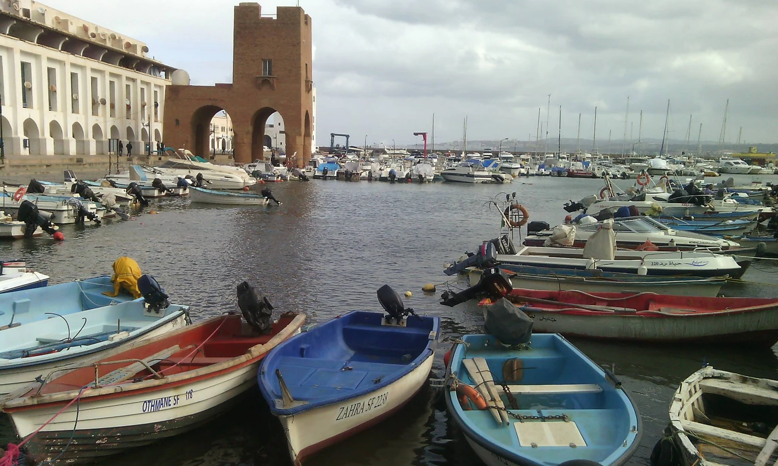 Barques colorées du port de Sidi Fredj devant la porte ocre à deux arches et les arcades blanches