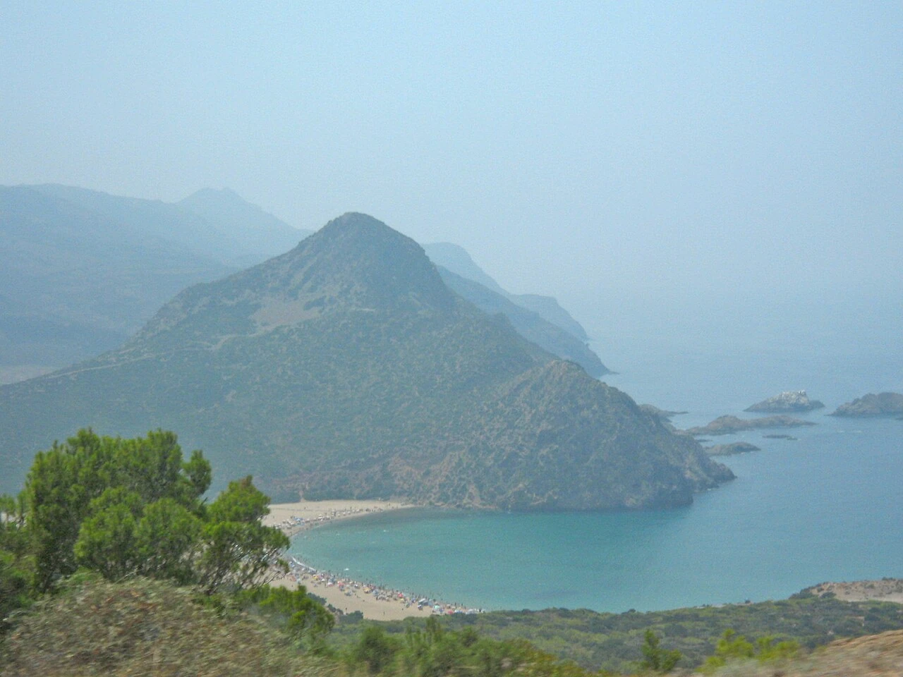 Vue en hauteur de la plage de Madagh, crique turquoise et promontoire rocheux.
