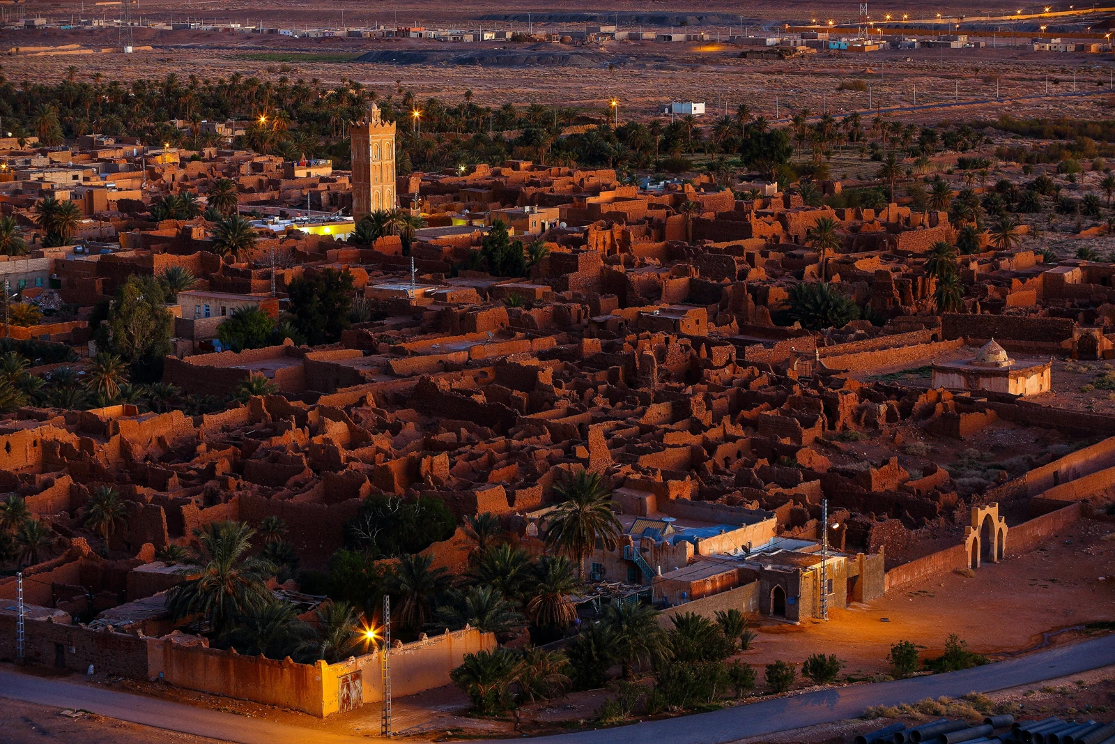 Vue du ksar de Kenadsa et de son minaret au crépuscule, entre murs de terre et palmeraie.