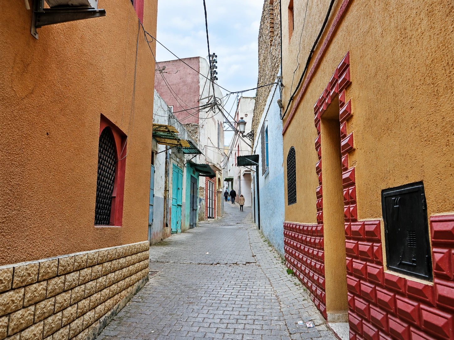 Ruelle de Tarbiaa à Nedroma, façades ocre, portes turquoise et encadrements rouges.