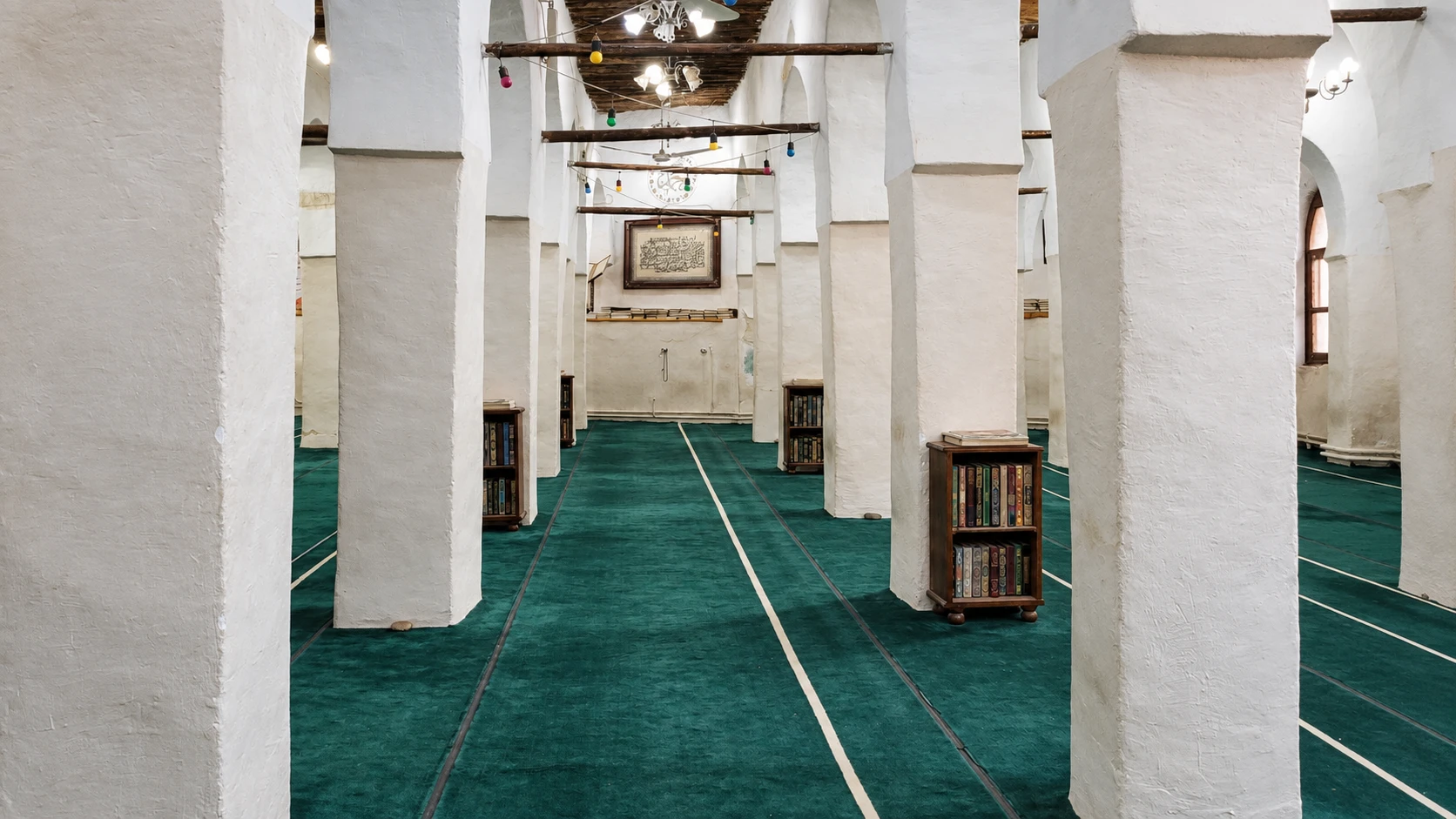 Illustration assistée par IA : Intérieur de la mosquée Sidi Thameur à Bou Saâda, avec piliers blancs, poutres en bois et tapis vert