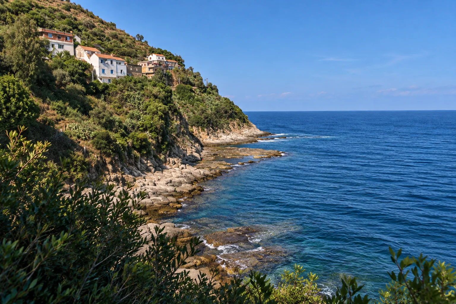 Une crique rocheuse de Collo, avec quelques maisons sur un versant boisé et la mer Méditerranée.