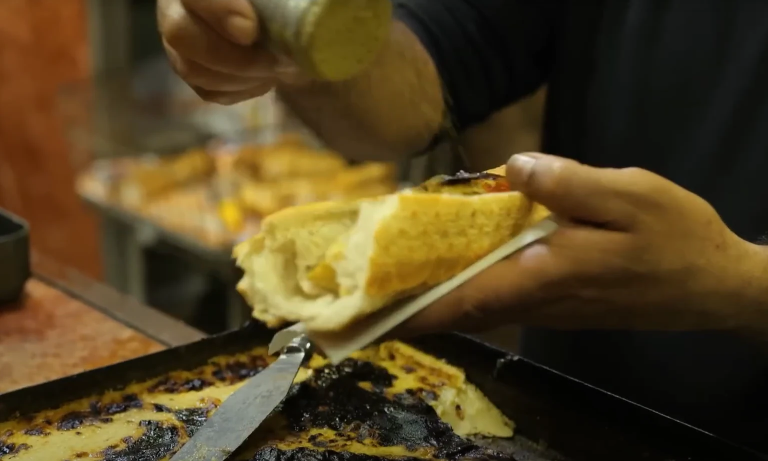Préparation d’un sandwich de calentica à Oran, servi dans du pain au-dessus du plat de pois chiches.