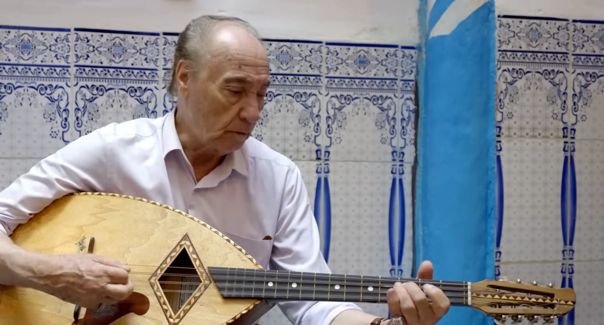 Abdelkader Chaou chante en jouant du mandole devant un mur de faïence à Alger.