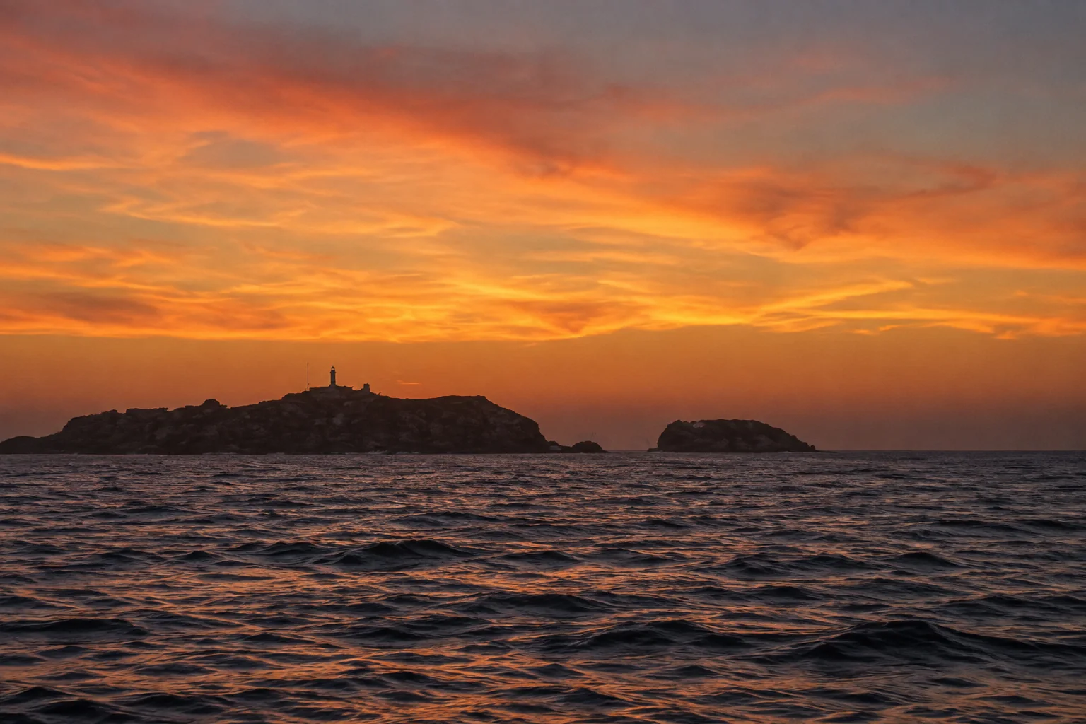 Les îles Habibas au crépuscule, avec le petit phare sur l'île principale et la mer au premier plan.