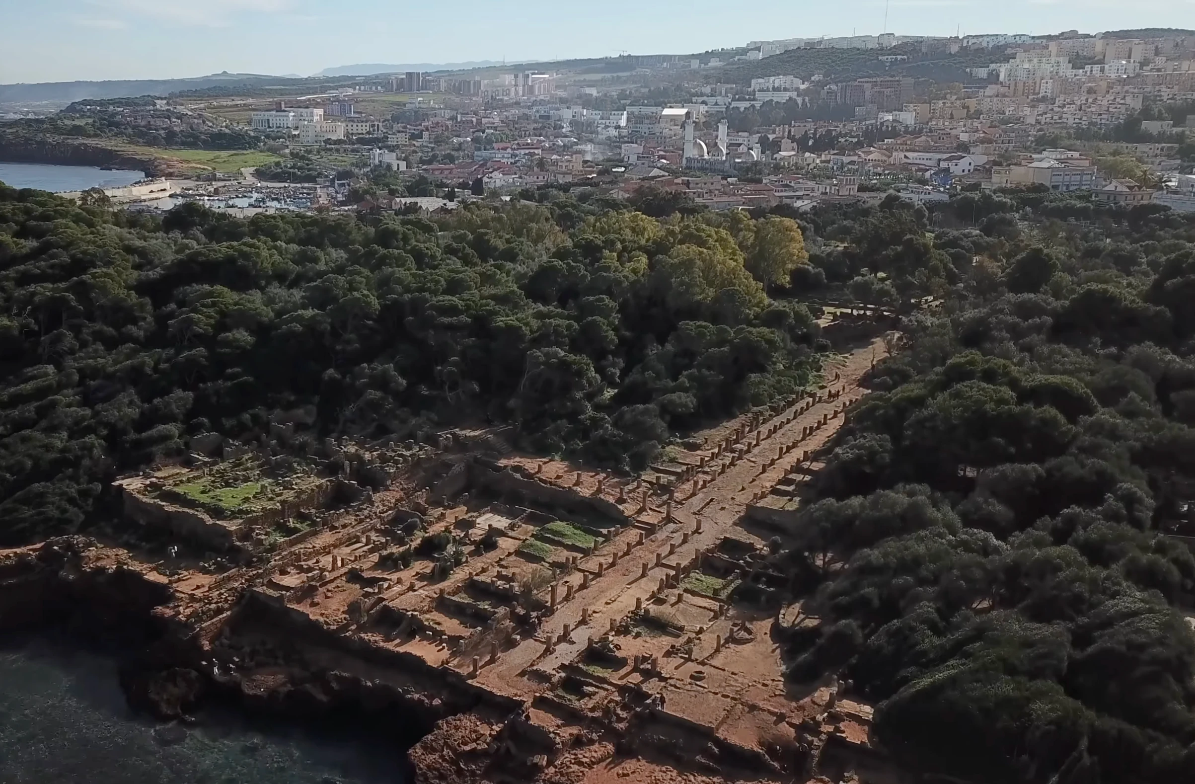 Vue aérienne des ruines antiques de Tipaza, avec le port et la ville en arrière-plan.
