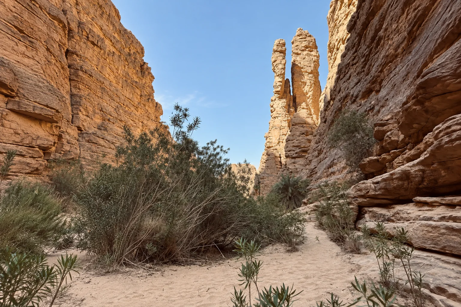 Un passage sableux entre les parois du canyon d’Essendilène et deux aiguilles rocheuses au fond.