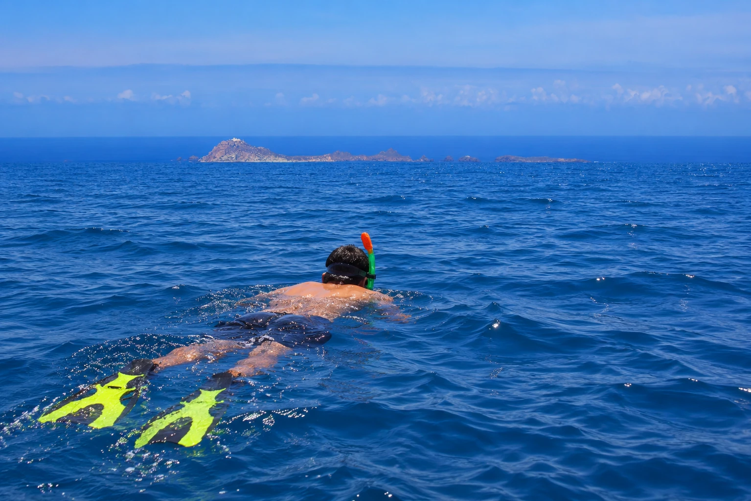 Un nageur équipé de masque, tuba et palmes dans la Méditerranée, avec la silhouette documentée des îles Habibas à l’horizon.