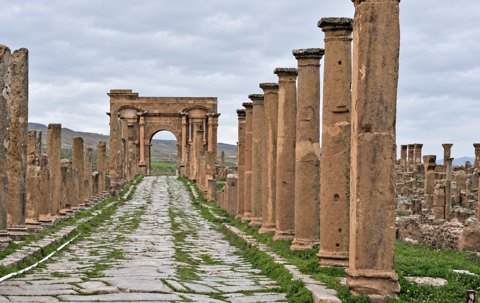 La voie pavée du decumanus de Timgad, bordée de colonnes, avec l’arc au fond.