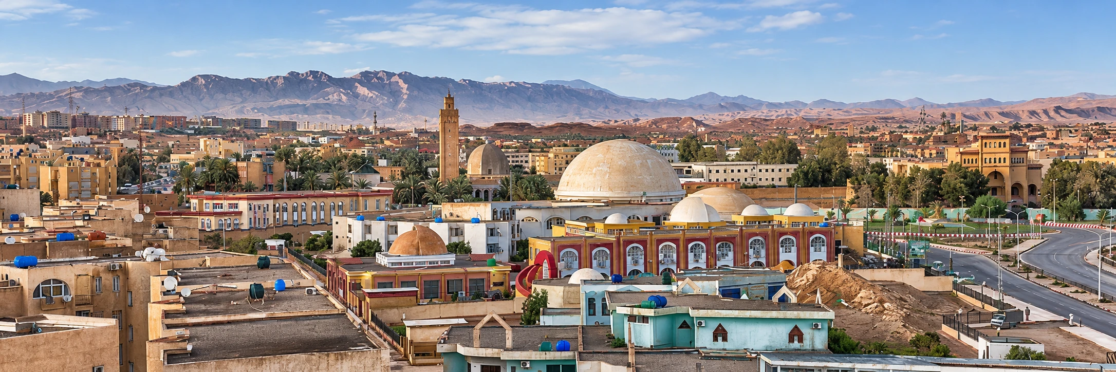 Le panorama de l’entrée ouest de Biskra, avec coupoles, minarets, maisons et montagnes au fond.