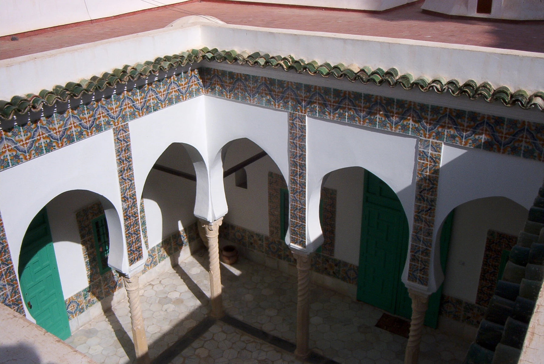 Patio de la villa Abd-el-Tif vu depuis la terrasse à l’étage, avec ses arcades, carreaux et portes vertes.