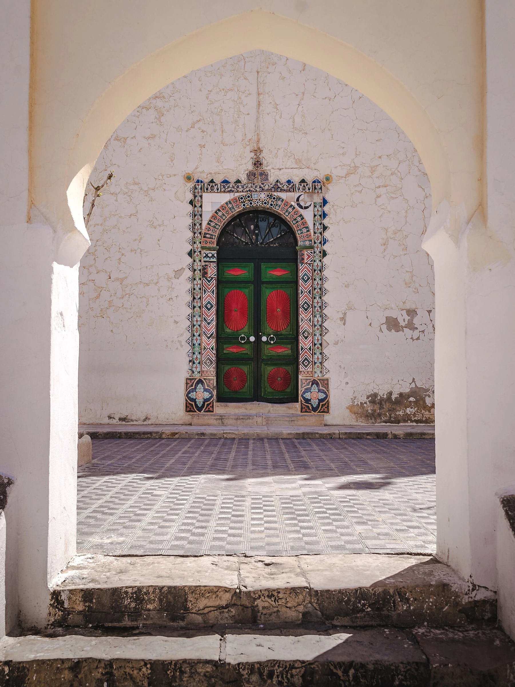 Entrée de la zaouïa d’El Hamel, porte verte et rouge entourée de faïences sous un grand arc blanc. Photographie réelle ; motifs conservés sans redessin.