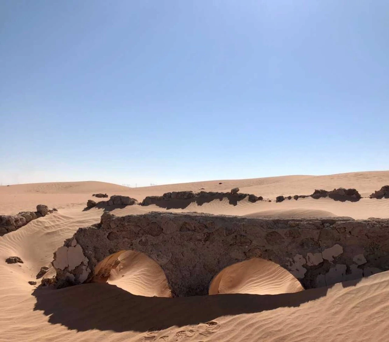 Deux arches et les murs ruinés de Sedrata partiellement recouverts de sable, photographie documentaire de Nassim Herket.
